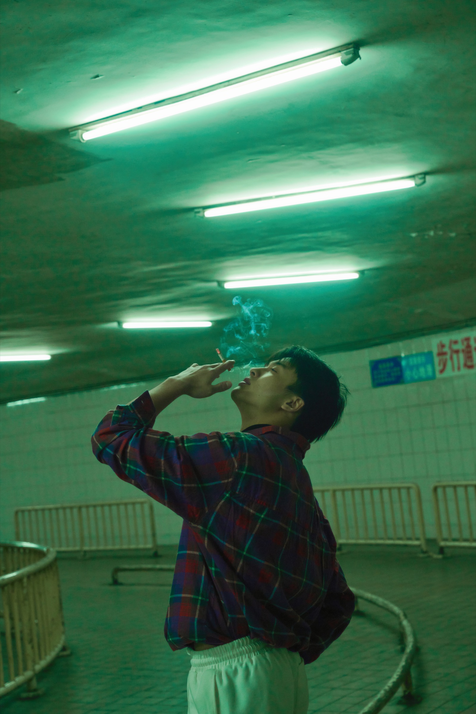 曾宇杰仰头吸烟，头顶是绿色荧光灯。